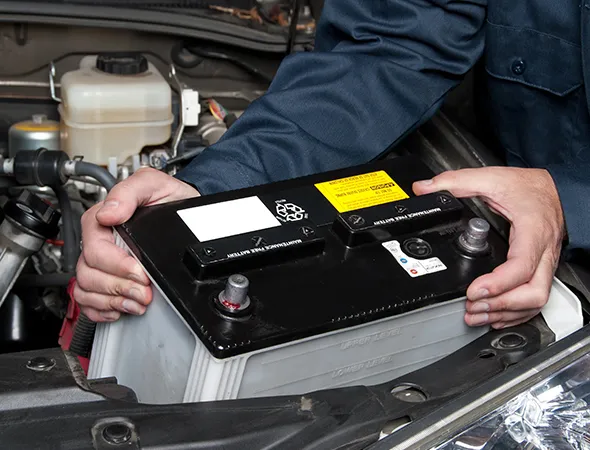 Hands of a mechanic installing a car battery under the hood, showcasing automotive repair. The scene conveys a sense of expertise and focus.