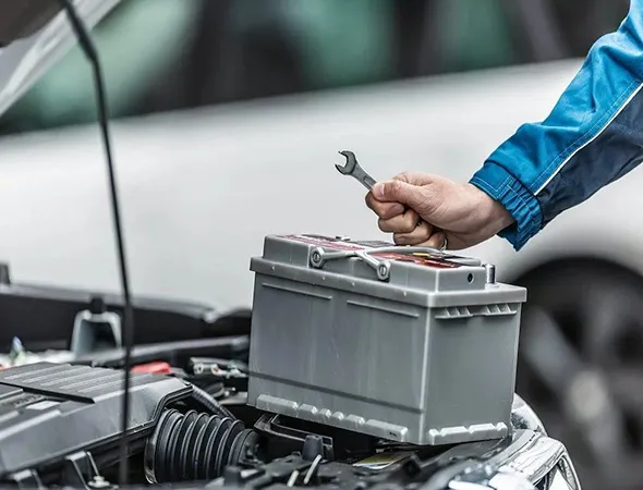 A man holds a wrench over the car's hood, engaged in the task of replacing the vehicle's battery.
