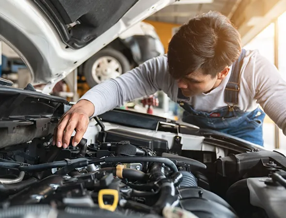 A mechanic in overalls focuses intently on repairing a car engine in a well-lit garage. The atmosphere is diligent and professional.