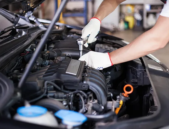 A mechanic wearing white gloves uses a socket wrench on a car engine in a garage. The setting conveys a sense of focus and technical work.